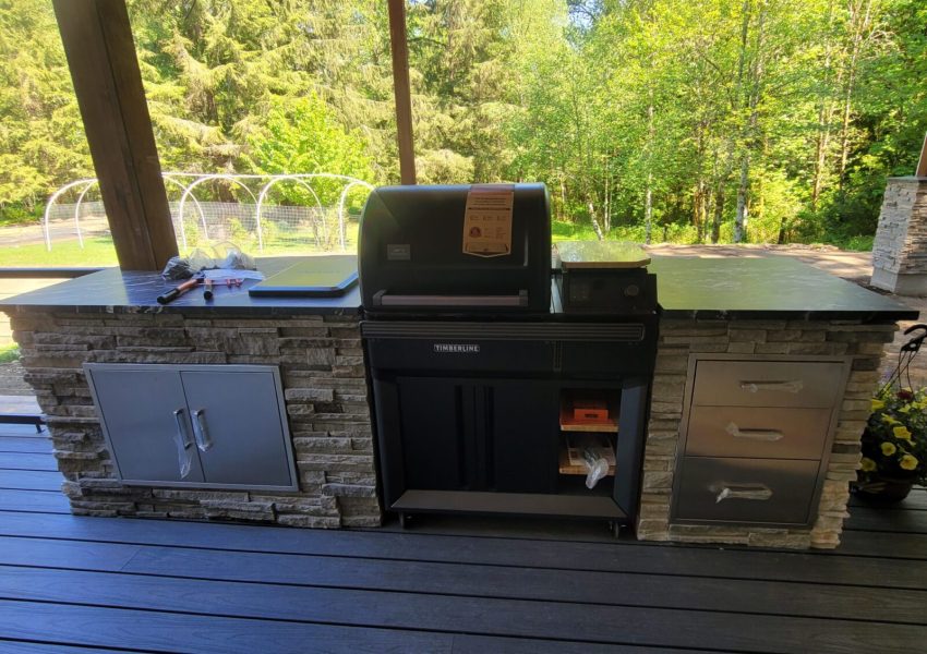 An Outdoor cooking space on a deck with a grill built into cabinets with countertops.