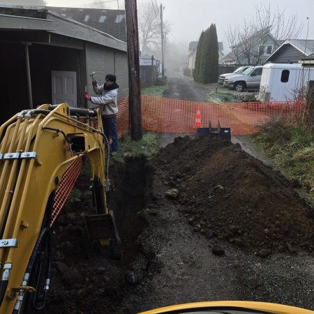 A worker and excavator making a trench for the utilities.